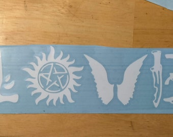 May include: A blue sticker with white cutouts of a winged angel, a pentagram inside a circle with rays, a knife, a gun, and a car. The word "LOVE" is spelled out using these cutouts.
