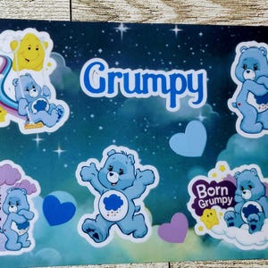 May include: A decorative placemat featuring a dark blue background with a starry sky design. It includes several cartoon bear characters in various poses, along with the word "Grumpy" and other text. The bears are primarily light blue with white accents.
