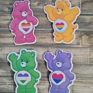 May include: Four Care Bear stickers with different colored fur and rainbow pride flags in their hearts. The bears are pink, yellow, green, and purple.