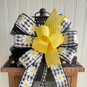 May include: A black and white gingham ribbon with white daisies, tied into a bow with a yellow polka dot ribbon. The bow is attached to a lantern.
