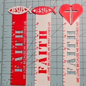 May include: Three red and white plastic rulers with a Christian theme. The first ruler has a red fish with the word "JESUS" inside. The second ruler has a white fish with the word "JESUS" inside. The third ruler has a red heart with a cross inside. All three rulers have the word "FAITH" and the text "WE LOVE BECAUSE HE FIRST LOVED US".
