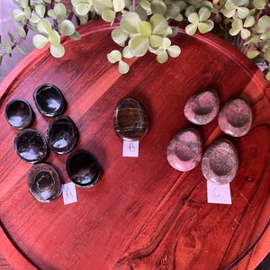 May include: A wooden tray with three sets of polished stones. Set A is black and has a shiny finish. Set B is a single tiger's eye stone. Set C is pink and green and has a rougher finish.