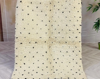 May include: A white and black Moroccan rug with a tufted texture and a geometric pattern. The rug has a fringe border.
