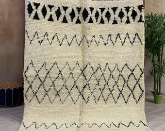 May include: A white and black Moroccan rug with a geometric pattern. The rug has a fringe border and is made of wool.
