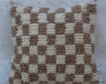 May include: A square-shaped throw pillow with a checkered pattern in beige and white. The pillow is made of a soft, fluffy material.