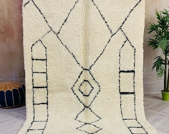 May include: A white Moroccan rug with a black geometric pattern. The rug has a fringe border and is made of wool.
