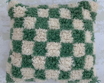 May include: A green and white checkered throw pillow with a fluffy texture. The pillow is made of a soft, plush material and has a checkered pattern.