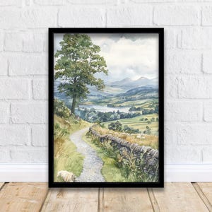 May include: Watercolor landscape art print in a black frame. The artwork depicts a winding path, stone wall, and a tree, leading to a lake and rolling hills under a cloudy sky. A sheep is resting on the path.