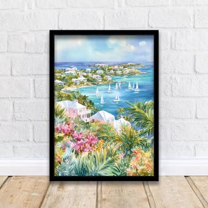 May include: Watercolour painting depicting a coastal scene with white houses, sailboats, and vibrant greenery. The artwork is framed in a black frame, set against a white brick wall and wooden floor.