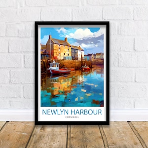 Puede incluir: Impresión artística enmarcada de Newlyn Harbour, Cornualles. La obra de arte representa una colorida escena portuaria con barcos, edificios y reflejos de agua. La impresión está en un marco negro y se muestra sobre un suelo de madera contra una pared de ladrillo blanco.