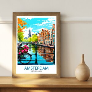 May include: A framed poster with a colorful illustration of a canal in Amsterdam, Netherlands. The poster features a bicycle with a basket of flowers, traditional buildings, and a blue sky with white clouds. The text "AMSTERDAM NETHERLANDS" is printed at the bottom of the poster.
