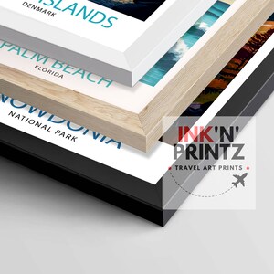 May include: Three framed travel art prints with a white, wood, and black frame. The prints feature the text "DENMARK ISLANDS", "PALM BEACH FLORIDA", and "SNOWDONIA NATIONAL PARK". The bottom frame has the text "INK'N' PRINTZ TRAVEL ART PRINTS" and a small airplane icon.
