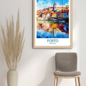 May include: A watercolor painting of the city of Porto, Portugal. The painting depicts colorful buildings along the Douro River with boats docked in the water. The painting is framed in a light wood frame.