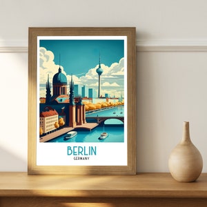 May include: A framed illustration of the Berlin skyline featuring the iconic Fernsehturm television tower, a dome-shaped building, and a bridge over a river. The illustration is in a vintage style with a blue, green, and yellow color palette. The text "BERLIN GERMANY" is printed below the illustration.