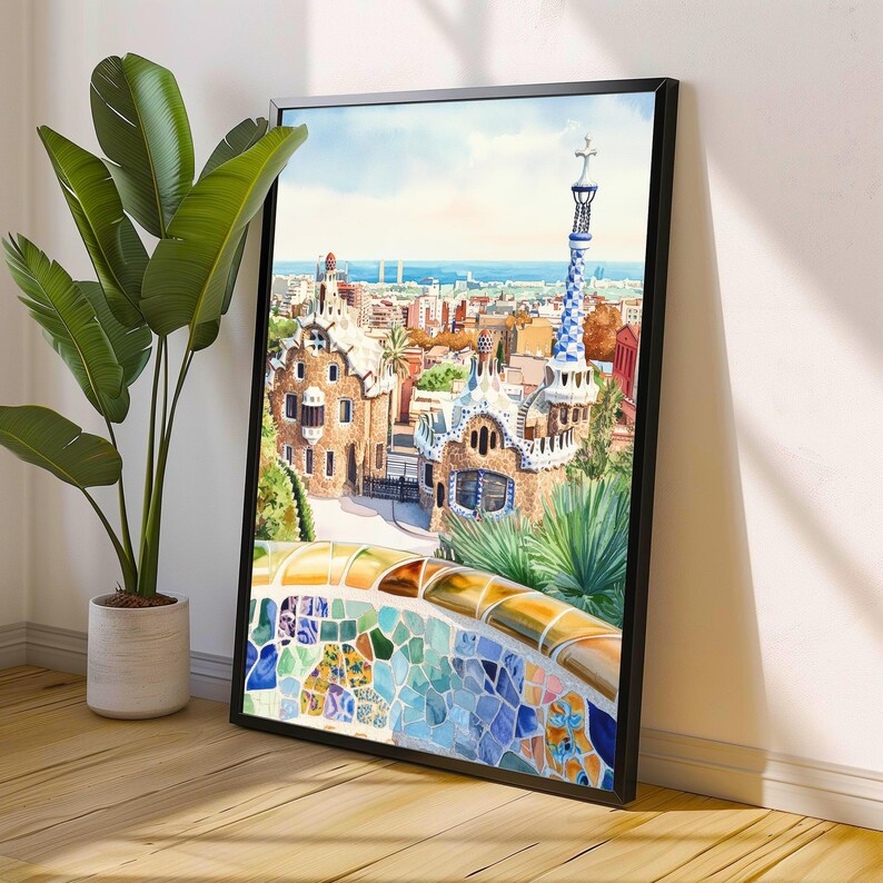 May include: A framed watercolor print of Park G&uuml;ell in Barcelona, Spain. The artwork depicts the park's unique architecture, including colorful mosaic benches and whimsical buildings. The sky is blue with a few clouds, and the print is displayed on a wooden floor.