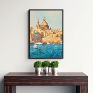 May include: Watercolor painting of a coastal city with a large domed building and a tall spire. The artwork features a vibrant blue sea and a cityscape in warm, earthy tones. The framed art is displayed on a dark wooden surface.
