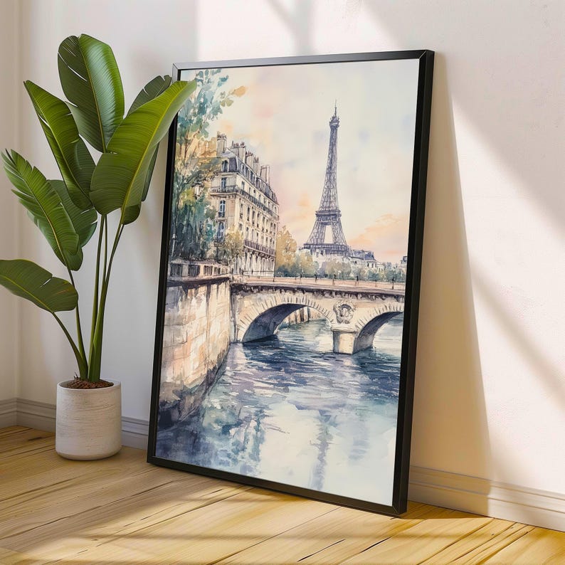 Op de afbeelding: Een aquarel schilderij van de Eiffeltoren in Parijs, Frankrijk. Het schilderij toont een brug over een rivier met gebouwen op de achtergrond. De lucht is zachtblauw met roze en oranje tinten.