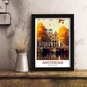 May include: A framed print of a vintage travel poster for Amsterdam, Netherlands. The poster features a colorful illustration of a canal with boats and buildings lined with trees in autumn colors. The text "AMSTERDAM" and "NETHERLANDS" is printed in white on a red background.