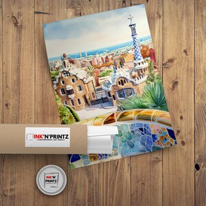 May include: Watercolor print of a cityscape with a distinctive architectural style, featuring a tall, patterned tower and mosaic details. The print is partially rolled and packaged in a brown tube with the "INK'N'PRINTZ" logo. A small, round tin with the same logo is also visible.