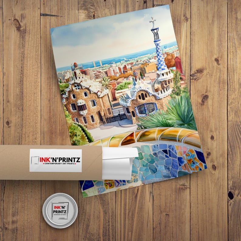 May include: Watercolor print of a cityscape with a distinctive architectural style, featuring a tall, patterned tower and mosaic details. The print is partially rolled and packaged in a brown tube with the "INK'N'PRINTZ" logo. A small, round tin with the same logo is also visible.