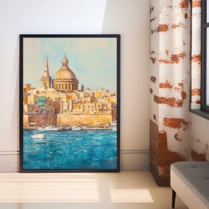 May include: A framed watercolor painting depicts a coastal city with a large domed structure and a tall spire. The artwork features a vibrant blue sea and a light blue sky, with boats in the water. The buildings are painted in shades of yellow and beige.