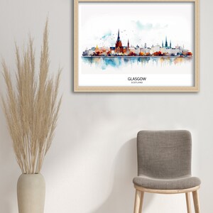 May include: A watercolor painting of the Glasgow skyline, featuring the city's iconic buildings and a reflection in the water. The painting is framed in a light wood frame and is titled "GLASGOW, SCOTLAND".