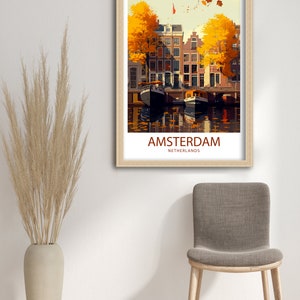 May include: A vintage travel poster featuring a colorful illustration of Amsterdam, Netherlands. The poster depicts a canal with boats and buildings lined with trees with yellow leaves. The text "AMSTERDAM" and "NETHERLANDS" is printed in red at the bottom of the poster.