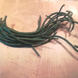 May include: A bunch of long, thin, green string beans on a light wood surface.