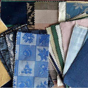 May include: A selection of fabric swatches in diverse colours and patterns. Features blue floral, striped, and solid fabrics. The swatches have varied textures and are arranged in a layered composition. A solid navy blue swatch has the number 1 in white.