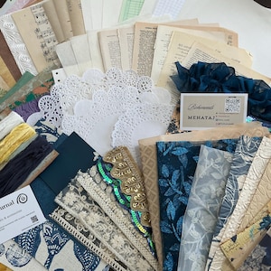 May include: A collection of craft supplies including vintage paper sheets, white lace doilies, blue fabric scraps, gold sequin trim, and ribbons. Two business cards are visible, one labelled Nabel My Journal and the other labelled Beheneds MEHATAJ.