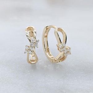 May include: A pair of gold hoop earrings with a delicate, intertwined design and small, clear cubic zirconia stones.