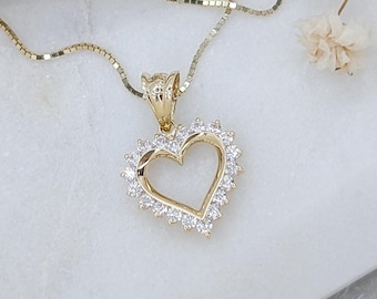 May include: A gold chain necklace with a heart-shaped pendant. The pendant is made of gold and has a clear crystal border.