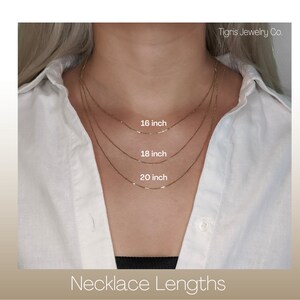 Puede incluir: Primer plano de una persona que lleva una camisa blanca, mostrando tres collares de oro de diferentes longitudes: 40 cm, 45 cm y 50 cm. El texto "Tigris Jewelry Co." aparece en la esquina superior derecha, y el texto "Necklace Lengths" est&aacute; en la parte inferior de la imagen.
