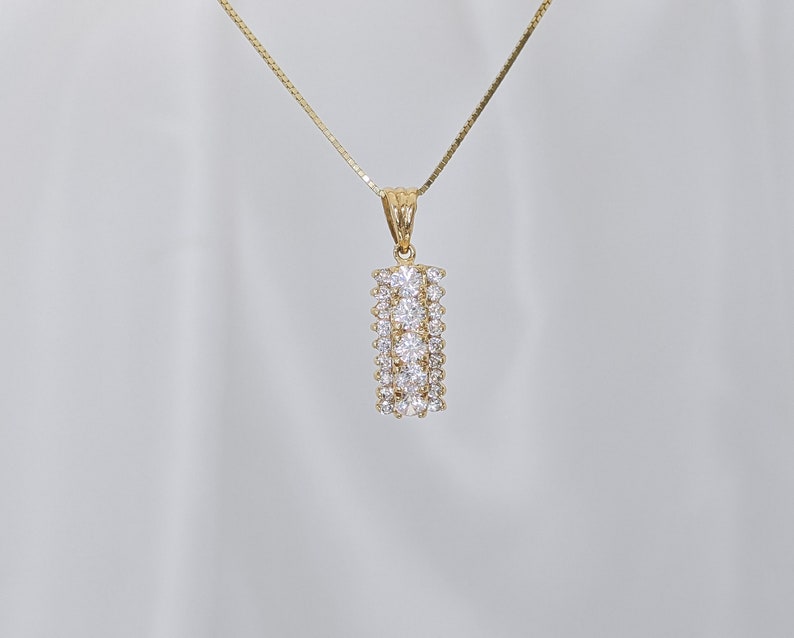 May include: A gold chain necklace with a pendant featuring a rectangular shape with multiple rows of clear cubic zirconia stones.
