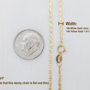May include: A delicate gold chain necklace with a clasp. The chain is flat and thin, and the width is 2mm for 14k white gold and 1.8-1.9mm for 14k yellow gold. The chain is shown next to a US dime for size comparison.
