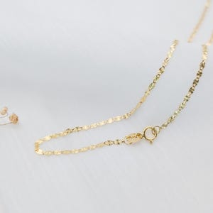 May include: A delicate gold chain necklace with a small clasp. The chain is made of tiny, linked, flat, oval-shaped pieces.