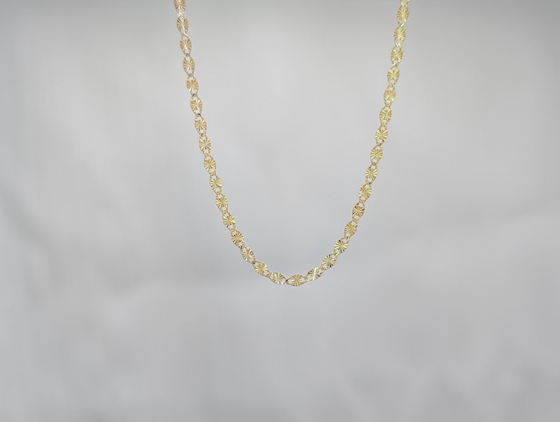 May include: A gold chain necklace with a delicate, patterned design. The chain is made of small, oval-shaped links.