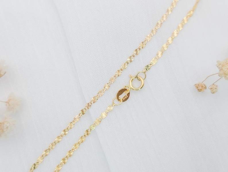 May include: A gold chain necklace with a delicate, floral pattern. The chain is made of small, interconnected flower-shaped links.