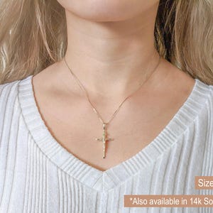 May include: A gold-colored cross pendant necklace. The cross features a detailed depiction of Jesus. The necklace is displayed on a person wearing a white ribbed sweater. Text on the image reads "Size Large" and "Also available in 14K Solid Gold."