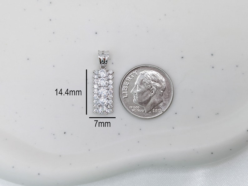 Puede incluir: Un colgante de plata con forma rectangular y una fila de piedras de circonita c&uacute;bica transparentes. El colgante mide 14,4 mm de alto y 7 mm de ancho.