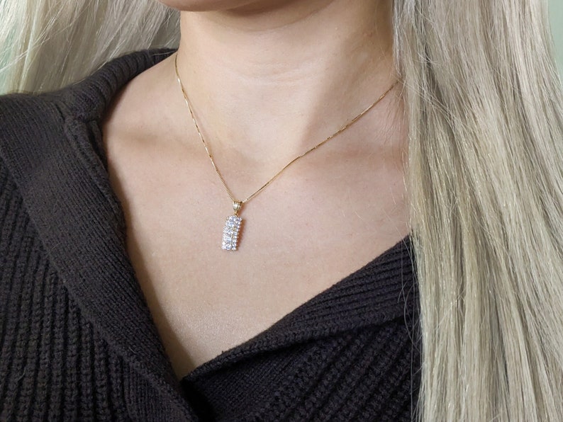 Puede incluir: Un collar de cadena de oro con un peque&ntilde;o colgante rectangular engastado con piedras de circonita c&uacute;bica transparentes.