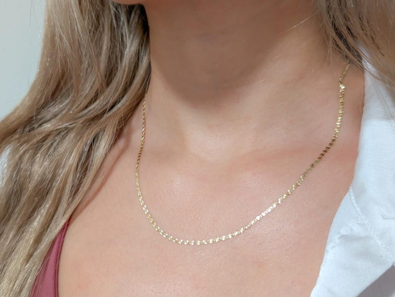 May include: A delicate gold chain necklace with a simple design. The chain is made of small, round links and is about 18 inches long.