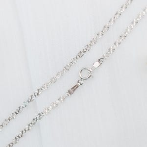 May include: A silver chain necklace with a delicate, floral pattern. The chain is made of small, interconnected links that create a delicate and feminine look.