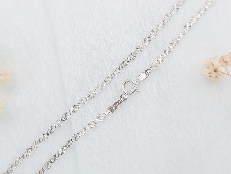 May include: A silver chain necklace with a delicate, floral pattern. The chain is made of small, interconnected links that create a delicate and feminine look.