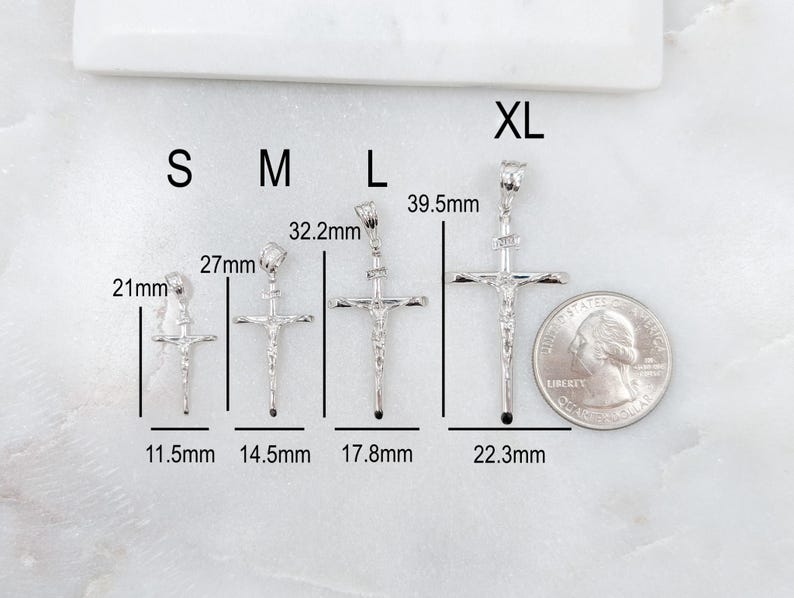 May include: A collection of silver crucifix pendants in various sizes, labeled S, M, L, and XL. Measurements are provided in millimeters, with the smallest pendant at 21mm and the largest at 39.5mm. A US quarter is included for size comparison.