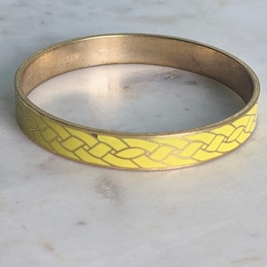Op de afbeelding: Een gouden armband met een geel gevlochten ontwerp.