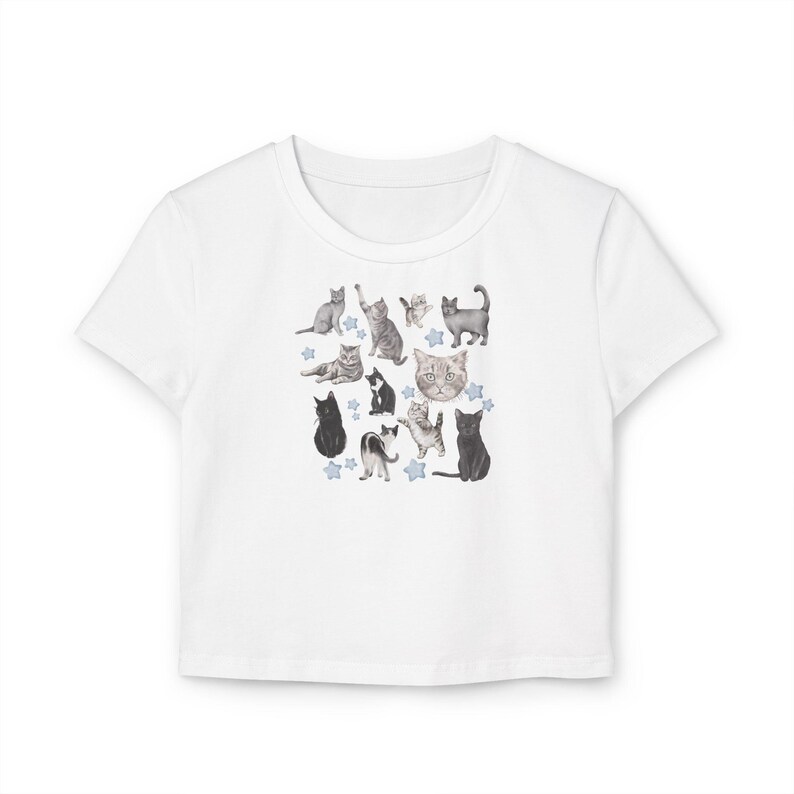 May include: White cropped t-shirt with a print of various cats in different poses. The cats are in shades of gray and black, and there are small blue stars scattered around them.