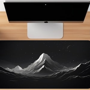 May include: A black and white minimalist mountain range design on a black mousepad. The design features a large mountain in the center with smaller mountains on either side. The background is a black starry night.