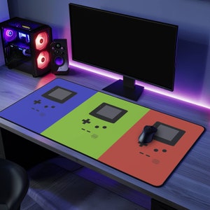 May include: A large gaming mouse pad with a colorful design featuring three retro video game consoles. The mouse pad is blue, green, and red with a black and white image of a handheld game console on each section.