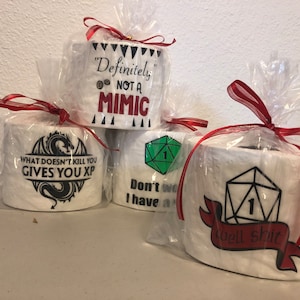 May include: Four rolls of toilet paper wrapped in clear plastic with red ribbon. Each roll has a different design with a Dungeons and Dragons theme. One roll has a dragon with the text "What doesn't kill you gives you XP". Another roll has a green 20-sided die with the text "Don't worry I have a 1". A third roll has a red 20-sided die with the text "Well Shit". The last roll has the text "Definitely not a mimic".